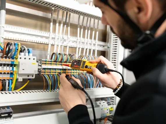 Elektroinstallateur-misst-im-schaltkasten Ein Elektroinstallateur misst Spannungen in einem Schaltschrank